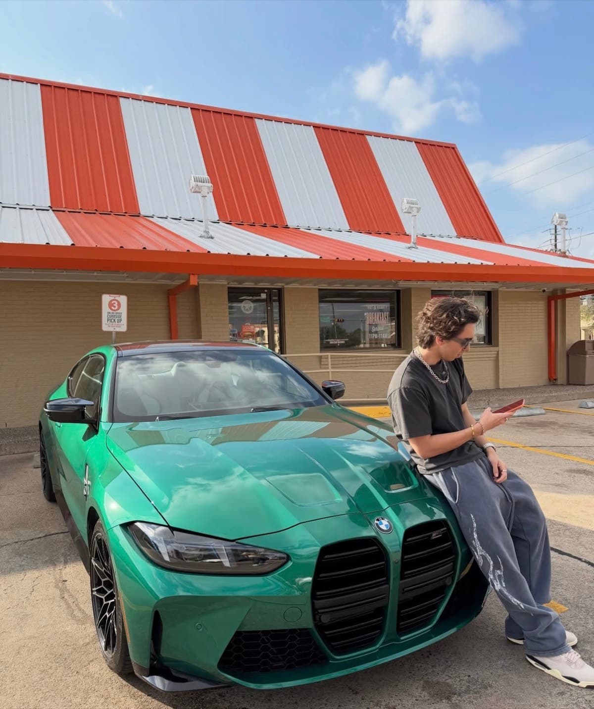 Aaron sitting on the hood of his green BMW M4 outside a Whataburger in Houston